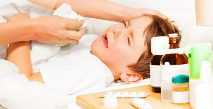 Barn med feber vilar i sängen bredvid febernedsättande läkemedel.