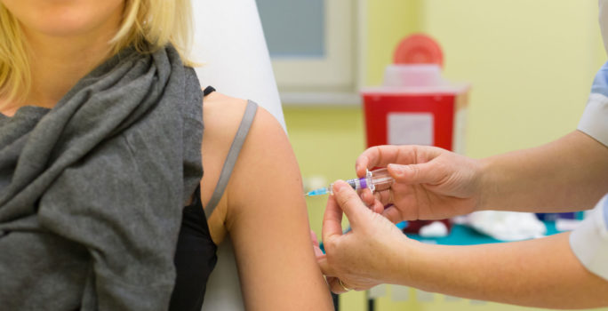 Kvinna får vaccin mot influensa på vårdmottagning.