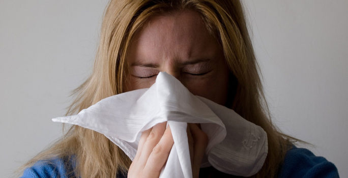 Kvinna med symptom på långvarig förkylning snyter sig i näsduk.