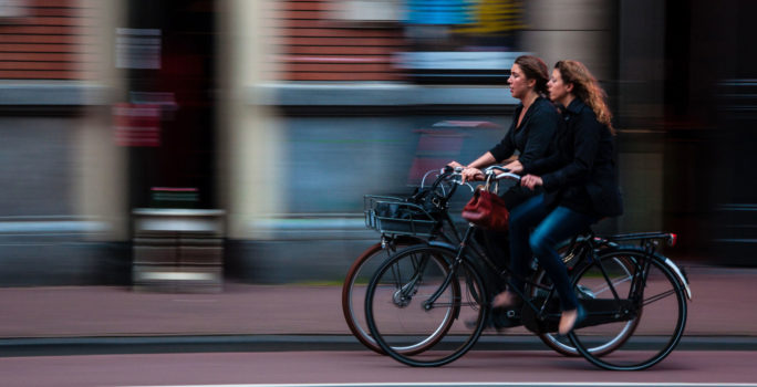 Två kvinnor cyklar till jobbet, ett bra sätt att undvika förkylning.