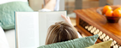 Caucasian woman reading a book lying on a sofa